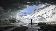 Valokuvaaja seisoo Morteratschin jäätikön luolan suuaukolla ihaillen lumisia vuoria ja kirkasta taivasta edessään.