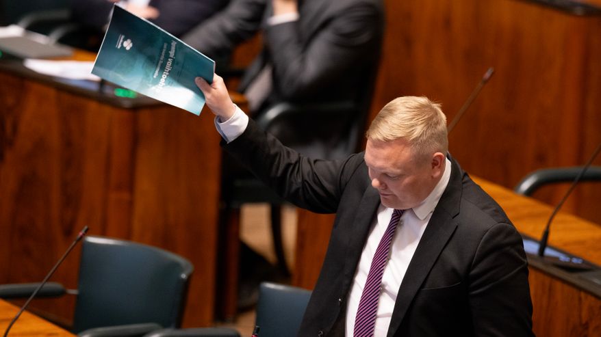 Antti Kurvinen heiluttaa keskustan vaihtoehtobudjettia eduskunnan istuntosalissa.
