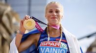 Alisa Vainio hymyilee kultamitali kädessään Suomen lippu hartioillaan.