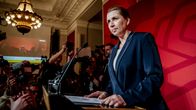 Poliitikko pitää lehdistötilaisuutta täydessä salissa median edustajien ympäröimänä.