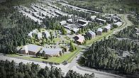 Flera byggnader och vägar syns i ett skogsområde med bostadshus och grönområden. I förgrunden, i en korsning, en affärsliknande större låg byggnad och en pylon.