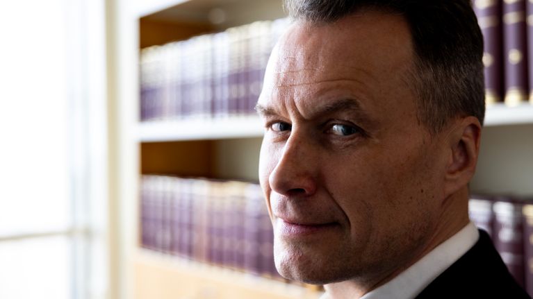 Toomas Kotkas katsoo kameraan, taustalla kirjahyllyssä kirjoja.