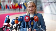 A blonde woman stands in front of media microphones. 