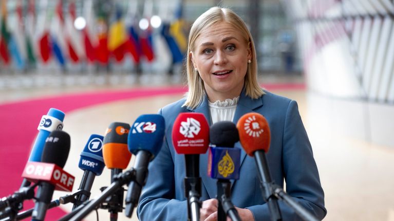 A blonde woman stands in front of media microphones. 