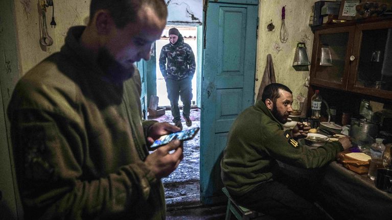 komentaja katsoo puhelintaan, kun ukrainalainen sotilas syö.