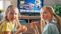 Två barn sitter framför en TV och äter snacks.