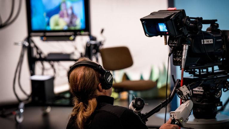 Henkilö kuulokkeet päässä tv-kameran takana.