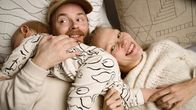 Muotoilijat Olli Sallinen ja Saana sipilä makoilevat nauravaisina sisustustyynyjen päällä. Vauva mönkii heidän päällään.