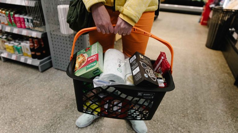 A woman holds a grocery basket in a food store. 
