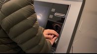 Mies suojaa toisella kädellä näppäimistöä pankkiautomaatilla.