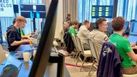 En grupp personer sitter vid datorer i ett konferensrum med flera bildskärmar och teknisk utrustning.