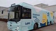 kirjastoauto pysäköitynä, asfalttia ja auton takana valkoinen kirjastotakennus 