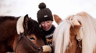 Kvinna i brun tröja står med två hästar som har huvudena i hennes famn.