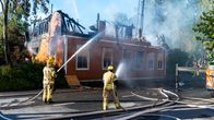 Brand i gult trähus i Karleby centrum. Två brandmän håller på med släckning och riktar brandslangar mot huset.