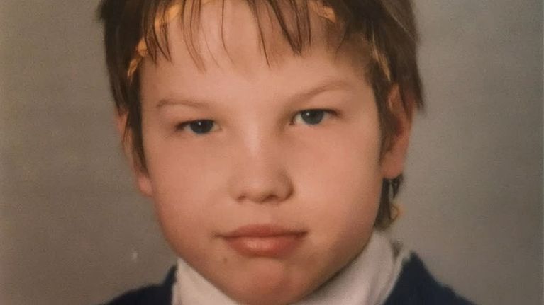 Ett skolfoto på en ung pojke som småler slugt mot kameran. 