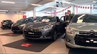 Uusia henkilöautoja autokaupan hallissa. Ostaja ja myyjä neuvottelevat.