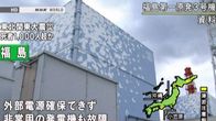 Fukushiman kolmosreaktori kuvattuna ulkoa, alakulmasta ylöspäin. Tummia pilviä taivaalla, Japanin tv:n tekstiä ja grafiikkaa kuvan päällä.