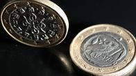 Portugalin ja Kreikan yhden euron kolikoiden takapuolet kuvattuna mustaa taustaa vasten. Portugalin kolikko on pystyssä, Kreikan kolikko makaa lappeellaan.