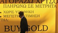 Iäkäs nainen panttilainaamon edustalla Ateenassa viime vuoden lopulla. Taustalla kreikankielisiä mainostekstejä sekä englanniksi: "BUY GOLD".