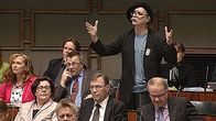 Pertti Virtanen puhuu eduskuntasalissa. Levittelee käsiään.