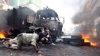 Hallitusta vastustavat mielenosoittajat suojautuvat kuorma-auton taakse Bangkokissa. Renkaita palaa kadulla.