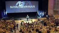 Kokoomuksen puheenjohtaja Jyrki Katainen puhuu puoluekokouksessa. Taustalla esitellään puolueen arvoja.