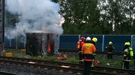 Sähkökeskus liekeissä radan varrella. Savua. Palomiehiä sammuttamassa paloa.