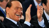 Italian pääministeri Silvio Berlusconi nauraa ja taputtaa käsiään konferenssin yleisössä.