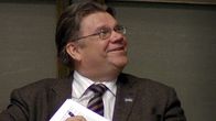 Perussuomalaisten puheenjohtaja Timo Soini istuu eduskuntasalissa ja hymyilee.