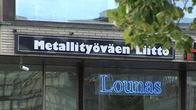 Metallityöväen liiton logo, jonka alapuolella neonkyltti "Lounas".