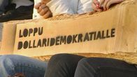 Lankun pätkä, jossa lukee "Loppu dollaridemokratialle" -teksti stencil-tyyliin sumutettuna mustalla spray-maalilla.