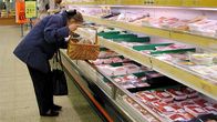 Nainen tutkii lihatuotteita marketin tiskillä.