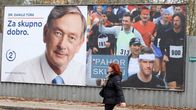Nainen kävelee kadulla ohitse kahden suuren vaakamuotoisen vaaliimainoksen. Vasemmalla olevassa on Türkin kasvot valkoista taustaa vasten, oikealla presidenttiehdokas Pahor juoksee keskellä maratonjuoksijajoukkoa.