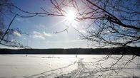 Aurinko paistaa järveen jään yllä.