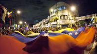 Ihmisjoukko ja valtava Venezuelan lippu Bolivar-aukiolla.