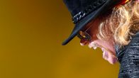 Axl Rose mustalierisessä hatussaan keltaisenoranssia taustaa vasten.