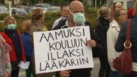 Mies osoittaa mieltään hengitysmaski suunsa edessä. Mielenosoituskyltissä lukee: "AAMUKSI KOULUUN ILLAKSI LÄÄKÄRIIN"