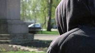 Huppupäinen ihminen istuu puiston penkillä.
