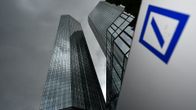 Kaksi pilvenpiirtäjää tummenevan taivaan alla Saksan Frankfurtissa. Etualalalla Deutsche Bankin logo.
