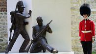 Brittisotilas punaisessa univormussa ja karvalakissa vartioi patsasta, joka esittää kahta 1800-luvun sotilasta.