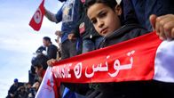 Pikkupoika pitelee huivia, jossa lukee "Tunisia" ranskaksi ja arabiaksi. 