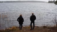 Suomussalmelaiset Oili ja Eero Keränen seisovat kotijärvensä rannalla. Keräset ovat vastustaneet Metsähallituksen hakkuusuunnitelmia Pesiöjärven saarissa. Saaret häämöttävät taustalla.