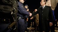 Ranskan presidentti François Hollande tarkastamassa turvallisuusjoukkojen riviä illalla. Hollande kättelee poliisia, joka on sinisessä univormussa, lippalakki päässään. Hollandella on musta päällystakki, musta kravatti. Kuvassa vasemmalla etualalla on toisen poliisin konepistooli, joka roikkuu varustevyöstä.