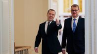 Venäjän pääministeri Dmitri Medvedev ja Suomen pääministeri Juha Sipilä tulevat suurista ovista. Miehillä on yllään mustat puvut, Sipilällä on sininen kravatti ja Medvedevillä tumma. Molemmat hymyilevät. Medvedev viittoo huoneen sisälle päin.