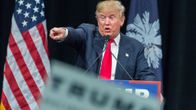 Donald Trump puhuu ja osoittaa oikealla kädellään jonnekin kuvaajasta takavasemmalle. Taustalla näkyy Yhdysvaltain lippu.