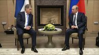 Niinistö ja Putin istuvat tuoleilla pienen pyöreän pöydän molemmin puolin. Niinistö puhuu juuri. Miesten taustalla ovat Suomen ja Venäjän liput. Pöydällä on kukka-asetelma.