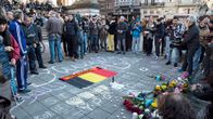 Ihmisiä kokoontuneena maassa olevan Belgian lipun ympärille Brysselissä.