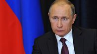 Putin katsoo vakavana kuvan vasenta reunaa kohti. Hänellä on tumma puku, tummanpunainen kravatti, jossa on sinistä kuviota. Taustalla näkyy Venäjän lippu.