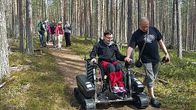 Nainen pyörätuolissa kulkee luonnossa telavaunun avulla 