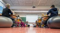 Koululuokka istuu pulpeteissa. Tunnistamattomia lapsia kuvattuna takaa.